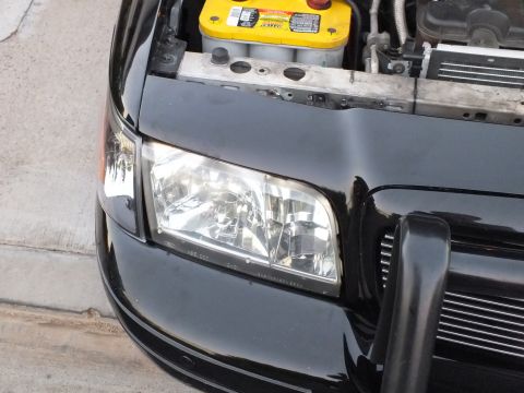 2003 Ford Crown Victoria - Clear-lens headlight seated in a black car front, battery and radiator visible.