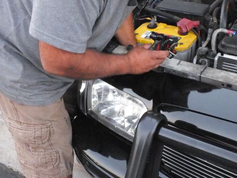 2003 Ford Crown Victoria - Person leans over the front of a black car installing a headlight near the battery.