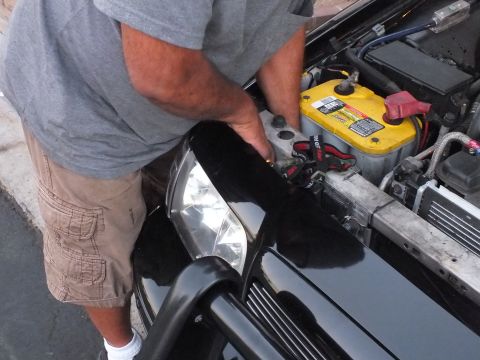 2003 Ford Crown Victoria - Person works at the front of a black car with battery and wiring exposed.