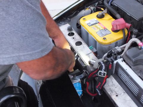 2003 Ford Crown Victoria - Close view of a person fastening hardware at a car core support beside the battery.