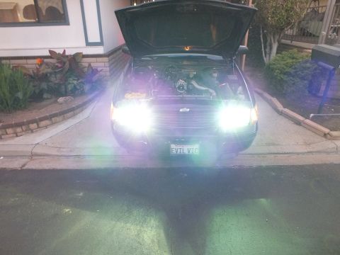2003 Ford Crown Victoria - Hood-up Crown Victoria glowing with HID conversion bulbs in a driveway after dark, EVIL VIC front plate visible