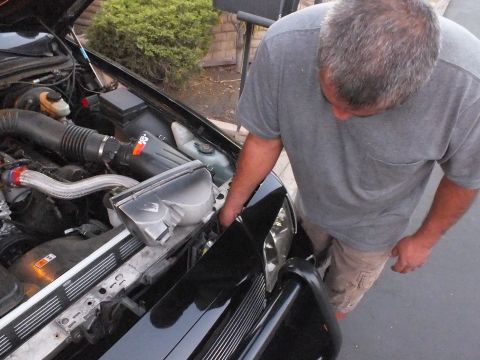 2003 Ford Crown Victoria - Gray-haired man working over the engine bay of the black Crown Victoria, air intake and alternator visible