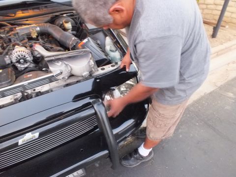 2003 Ford Crown Victoria - Mechanic leaning into the front corner of the Crown Victoria, billet grille and police push bar in frame