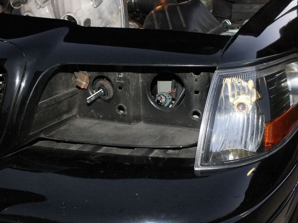 Empty headlight housing pocket on black Crown Victoria showing adjuster screws and wiring sockets