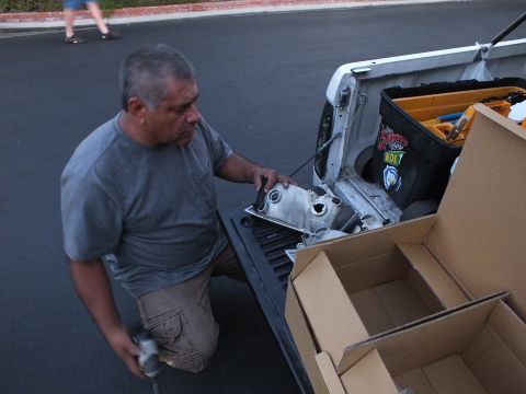 2003 Ford Crown Victoria - Man at a pickup tailgate inspecting an aluminum casting, parts box and tool bag laid out beside him