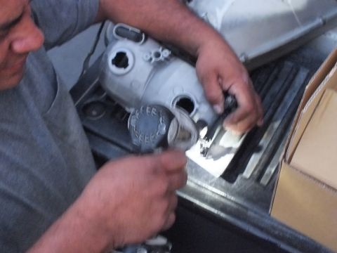 2003 Ford Crown Victoria - Hands gripping a primer-gray aluminum housing labeled COFFEE BEER while modifying it on the tailgate