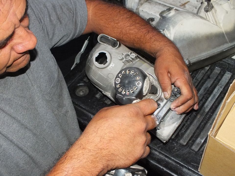 Man fitting a black gauge dial onto aluminum part on truck tailgate beside cardboard box