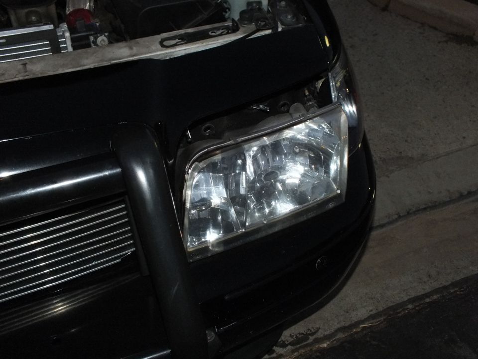 Clear multi-reflector headlight installed on black Crown Victoria front corner at night