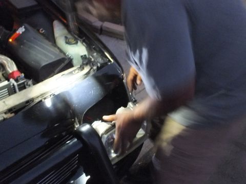 2003 Ford Crown Victoria - Motion-blurred mechanic reaching into the headlight area of the Crown Victoria under a bright work light