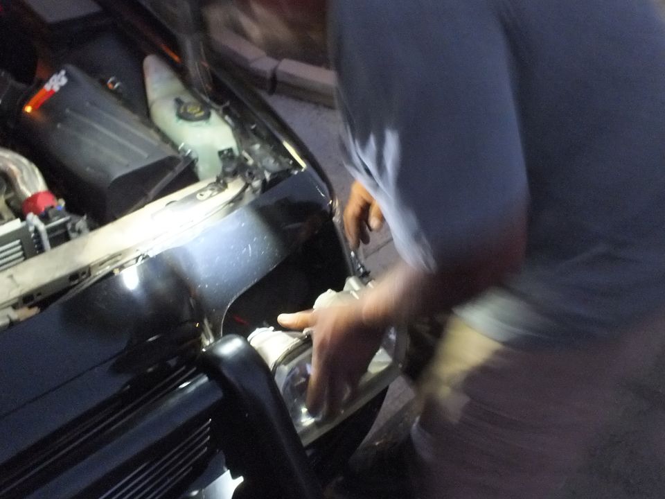 Blurred man reaching into front corner of black Crown Victoria lit by work light at night
