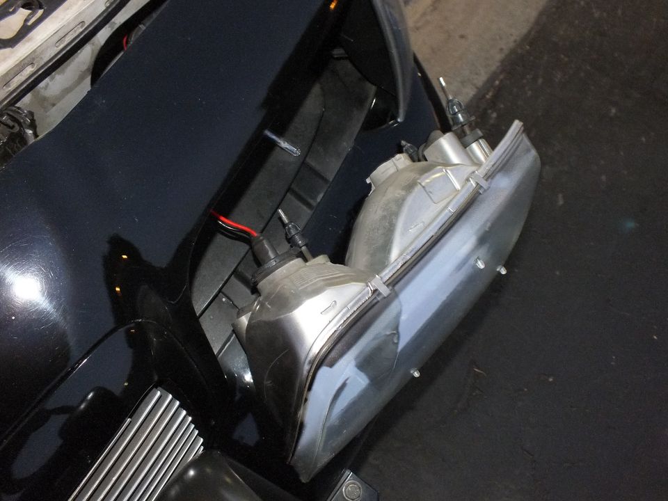 Two chrome multi-reflector headlight assemblies sitting in front corner of black Crown Victoria