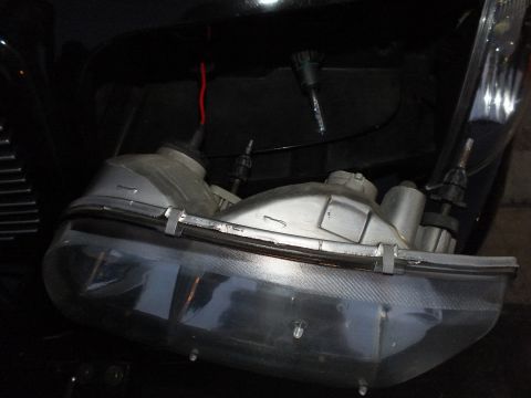2003 Ford Crown Victoria - Opened headlight housing with bulb holders and red wire laid across the dark Crown Victoria body