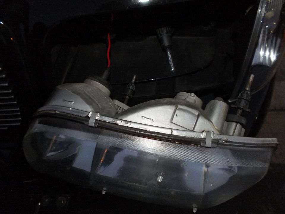 Disassembled headlight assembly with bulbs and wiring resting on black Crown Victoria front