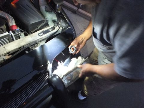 2003 Ford Crown Victoria - Man inserting a bulb into the Crown Victoria headlight, work light illuminating the engine bay edge