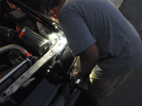 2003 Ford Crown Victoria - Hands reach into the front radiator support area of a car lit by a flashlight in the dark