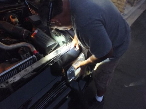2003 Ford Crown Victoria - Gloved hands position a headlight unit on a dark sedan with the hood up under a worklight
