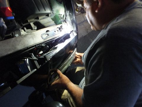 2003 Ford Crown Victoria - Top-down angle shows a worker leaning into the brightly lit front structure of a car in the dark
