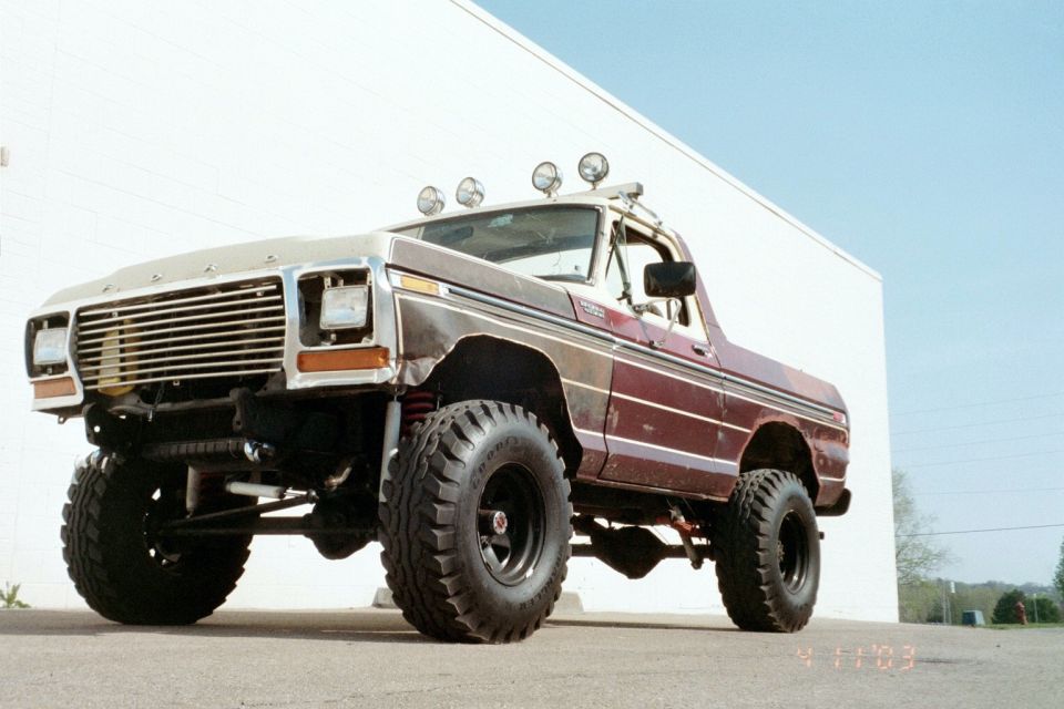 Front three-quarter low shot of a lifted maroon-and-tan Ford pickup with roll bar lights