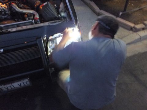 2003 Ford Crown Victoria - Man kneels at the front corner of a dark car showing a turbocharged engine bay and EVIL VIC plate