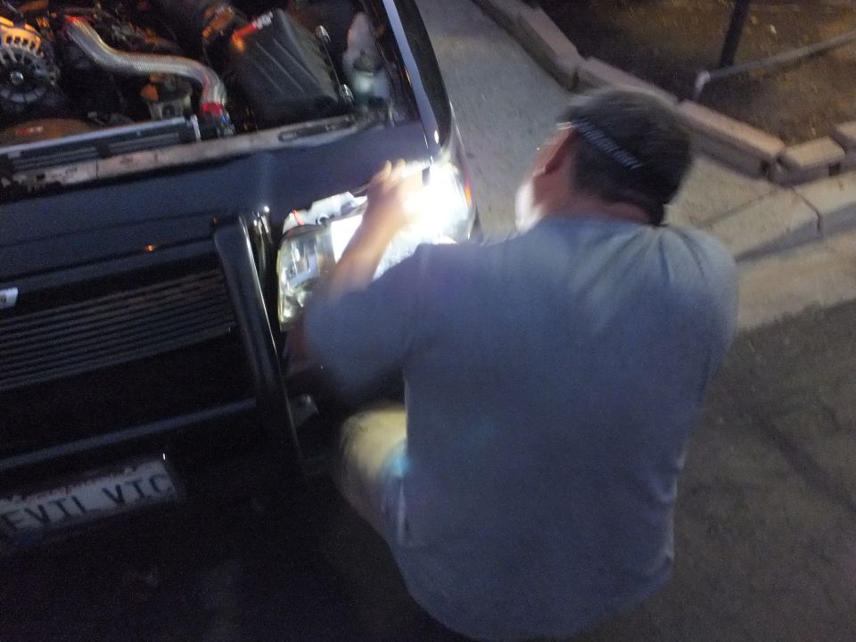 Worker kneeling at front of dark sedan with EVIL VIC plate and turbo engine bay