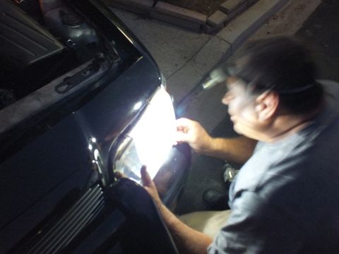 2003 Ford Crown Victoria - Worker reaches toward the glowing headlight of a dark car while crouching in the dark