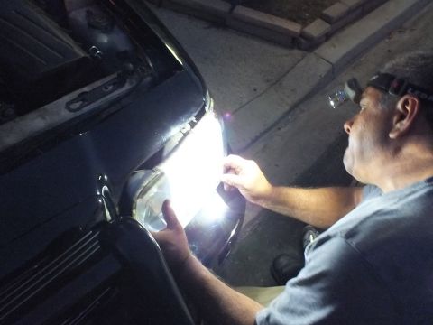 2003 Ford Crown Victoria - Hands set a round projector-style headlight into the front corner of a dark car under worklight