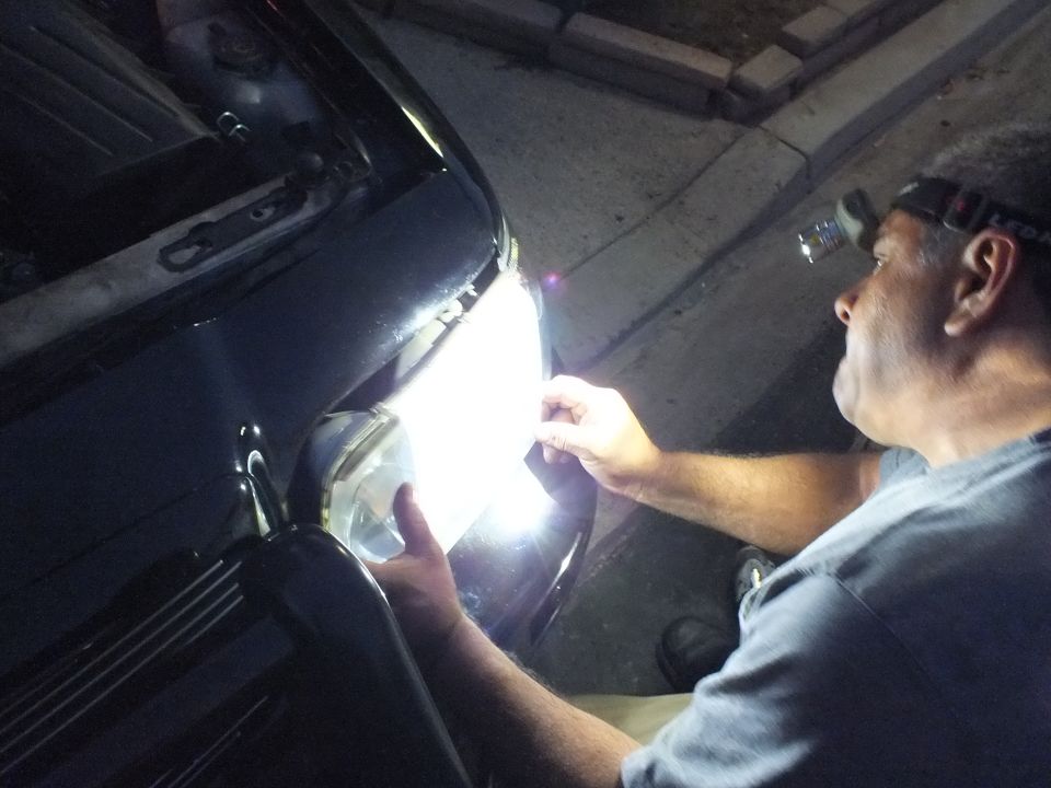 Worker adjusting round projector headlight on dark sedan at night