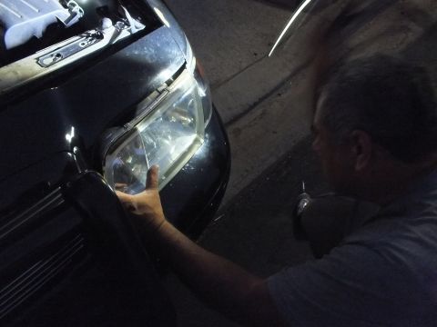 2003 Ford Crown Victoria - Worker removes or fits a headlight housing on the front fender of a dark car in the dark