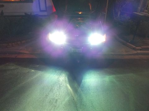 2003 Ford Crown Victoria - Dark car shines intense bluish-white headlights toward the camera in a nighttime driveway