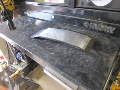 2008 Jeep Wrangler - A silver textured part rests on a black workbench, possibly for a vehicle.