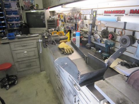 2008 Jeep Wrangler - A custom metal skid plate sits on a workbench in a workshop, surrounded by tools and storage.