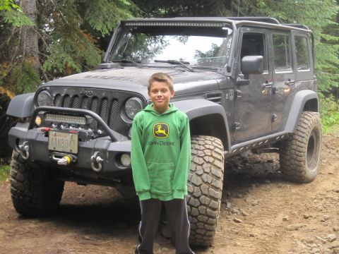 2008 Jeep Wrangler - A boy poses with a modified Jeep Wrangler on a dirt road surrounded by trees.