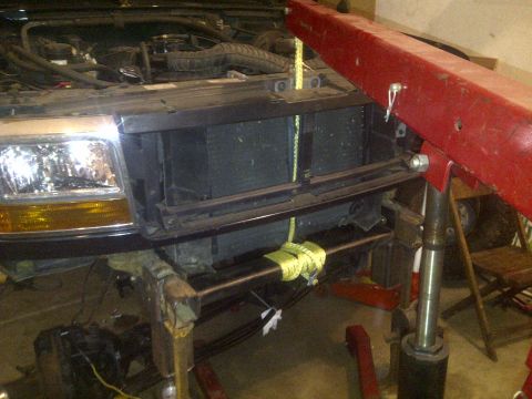 1995 Ford Bronco - Front view of a 1995 Ford Bronco undergoing repairs, with the hood open and an engine hoist positioned above.