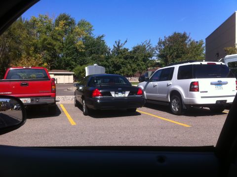 2003 Ford Crown Victoria - A black 2003 Ford Crown Victoria is parked between a red truck and a white SUV.