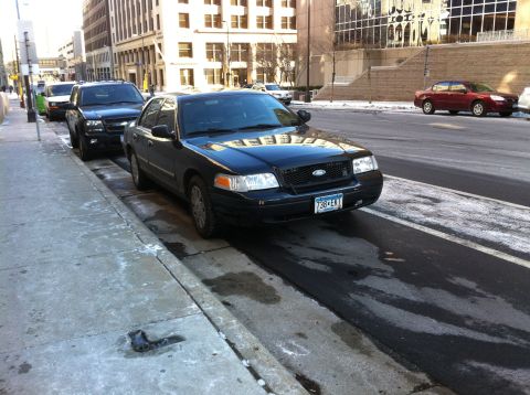 2003 Ford Crown Victoria - A black 2003 Ford Crown Victoria is parked on a city street, with other vehicles visible in the background.