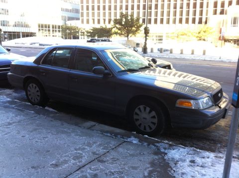 2003 Ford Crown Victoria - A dark gray 2003 Ford Crown Victoria is parked on a city street with snow and ice on the sidewalk.