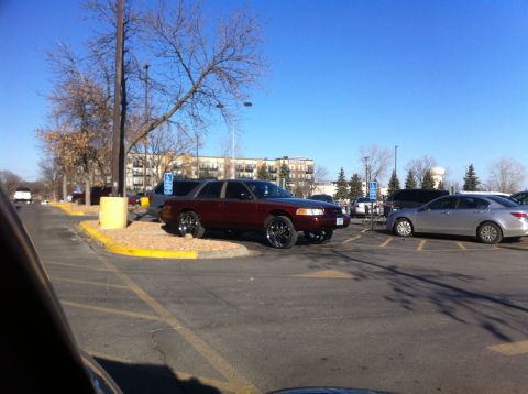 2003 Ford Crown Victoria - A maroon sedan with large chrome wheels is parked in a lot on a sunny day.