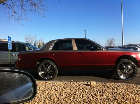 2003 Ford Crown Victoria - A two-tone 2003 Ford Crown Victoria is seen from the side, modified with oversized chrome wheels.