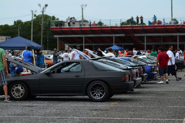 Matte black 1987 Mazda RX-7 parked in a row with other cars. Hood is open