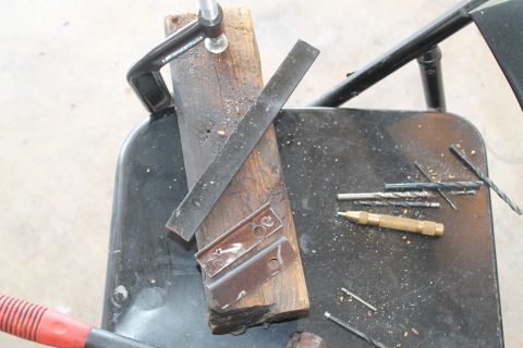1990 Ford Bronco - Metal brackets are being worked on with tools, including drill bits and a clamp.