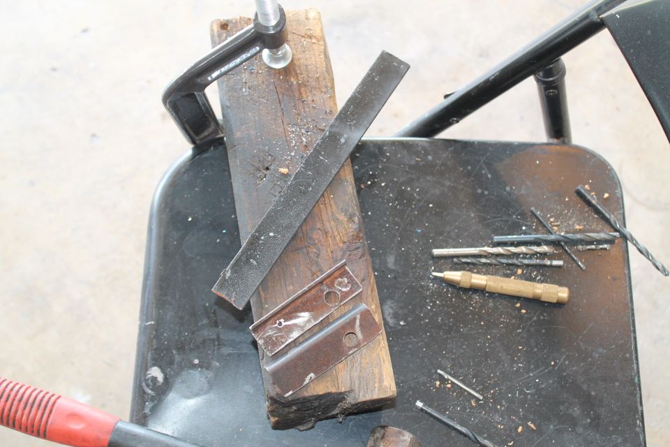 Metal brackets clamped to wood with drill bits and a punch nearby