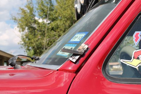 1990 Ford Bronco - Close-up of a red SUV's windshield corner, showing inspection stickers and a damaged mirror mount.