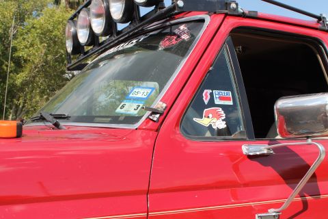 1990 Ford Bronco - Close-up of a red truck's front passenger side, roof-mounted lights and various stickers on the windows.
