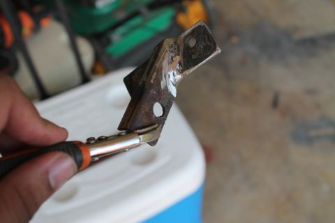 1990 Ford Bronco - A close-up of a rusty metal bracket being held by pliers, with a white cooler in the background.