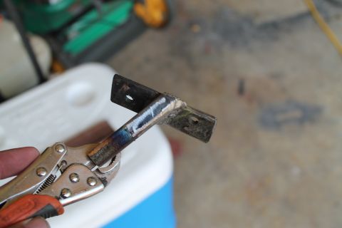 1990 Ford Bronco - A metal bracket is held by pliers, with a white cooler and green object in the background.