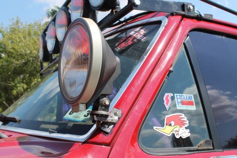 1990 Ford Bronco - Close-up of a red SUV's A-pillar light and various stickers on the windshield.