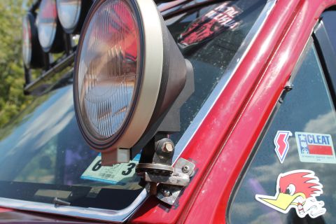 1990 Ford Bronco - Off-road light mounted on the A-pillar of a vehicle, with various stickers on the glass.