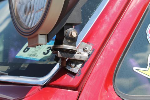 1990 Ford Bronco - A close-up shot focuses on the mounting hardware for an auxiliary light attached to the A-pillar of a red vehicle.