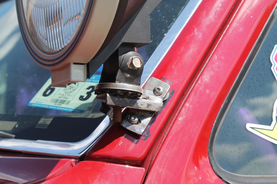 Close-up of a red vehicle's A-pillar showing a mounted auxiliary light and a sticker on the window