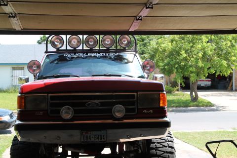 1990 Ford Bronco - Front view of a red 1990 Ford Bronco with multiple auxiliary lights and a "ROUGH COUNTRY" decal on the windshield.